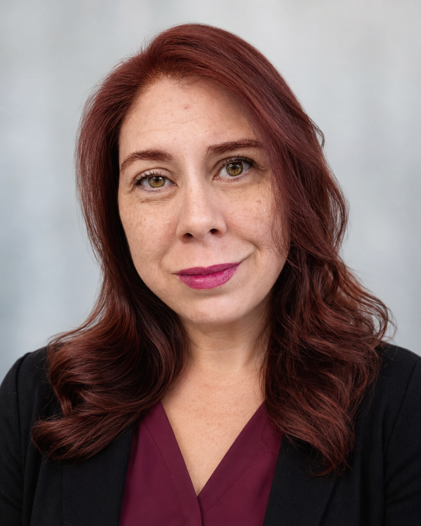 582ff564-906c-4e1b-933f-79ed1718b53f | Empowered Scholars Close-up portrait of a woman with shoulder-length auburn hair, wearing a burgundy top and black blazer, smiling softly against a neutral background.