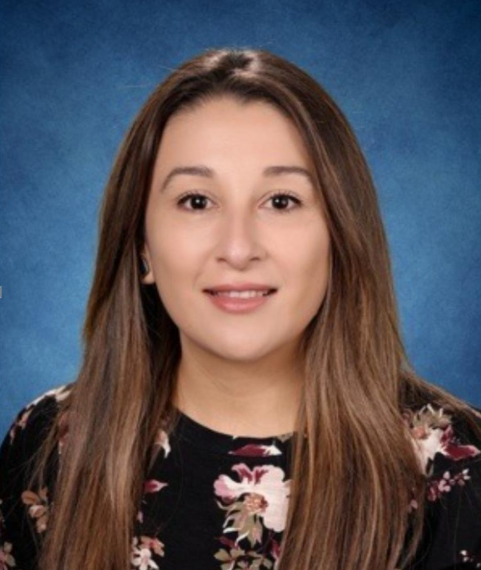 yesenia | Empowered Scholars Head-and-shoulders portrait of a smiling woman with long brown hair in a floral blouse, against a blue studio backdrop.